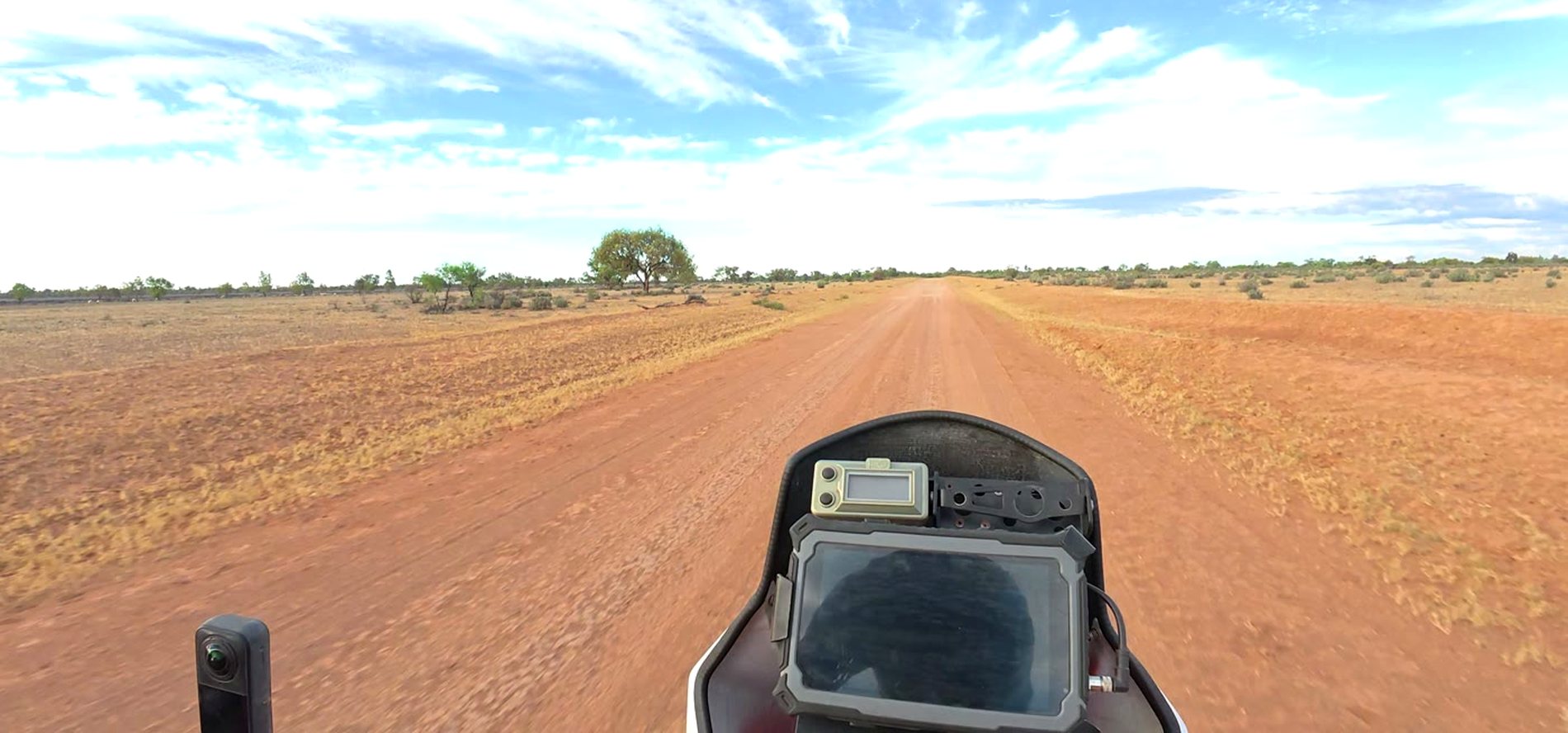 Rider point of view on a rally motorcycle, a red dirt track running dead straight to the horizon
